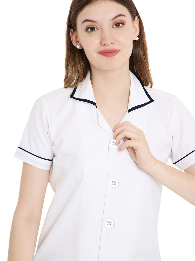 Woman wearing a women's white assistant apron top with navy piping and button closure, showcasing a professional nurse look.