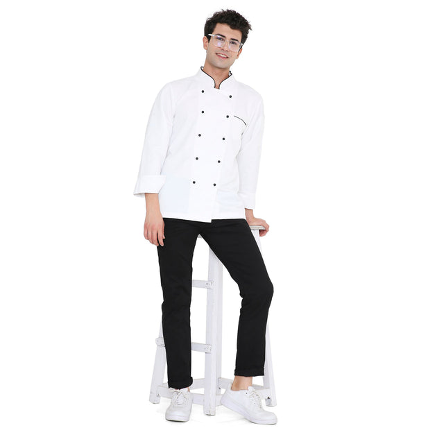 Unisex chef wearing a classic full sleeve chef coat with black accents, standing on a stool, showcasing style and functionality.